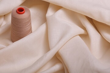 Summer fabric. Top down view of beige lightweight linen fabric with sewing thread resting atop. The...