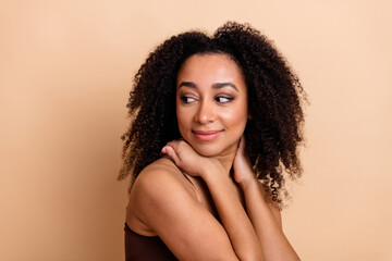 Portrait of a beautiful young woman with curly hair posing against a beige background, expressing...