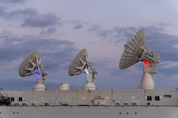 Three large satellite antennas on a ship deck, captured against a blue and pink evening sky....
