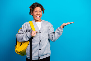 Cheerful schoolboy wearing gray cardigan and backpack, gesturing with enthusiasm against vibrant...