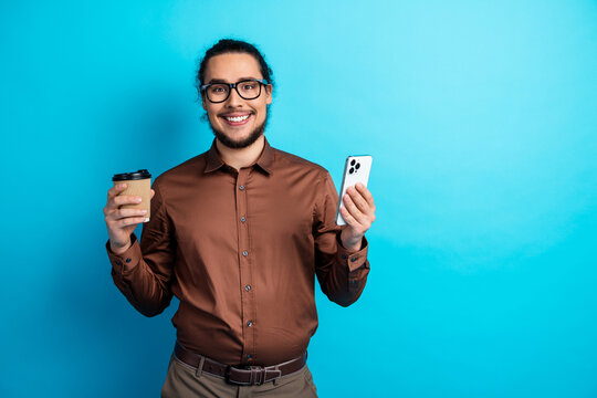 Confident young businessman holding coffee and smartphone against teal background showcasing professional lifestyle