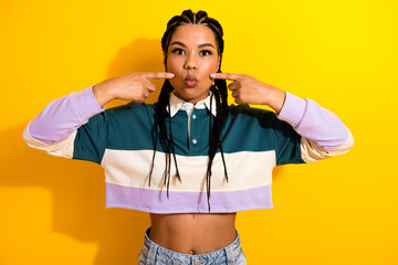 Vibrant young woman playfully posing against a bold yellow background in trendy fashion with...