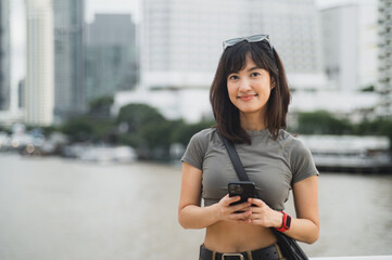 Happy young southeast asian woman teenager blogger using smartphone searching guide. World travel...