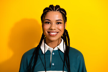 Portrait of a young woman with braided hair wearing a casual top against a bright yellow background