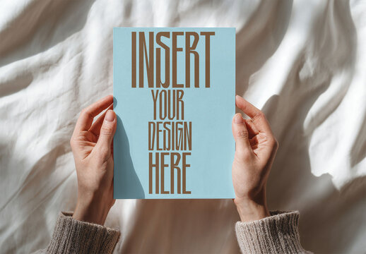 Hands display a blank A4 paper on a soft, light fabric surface. Perfect for design mockups or presentations.