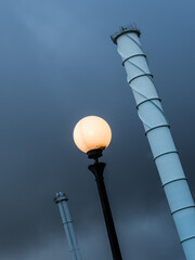 Lamppost illuminated under dark sky near smokestacks in Gothenburg capturing industrial atmosphere