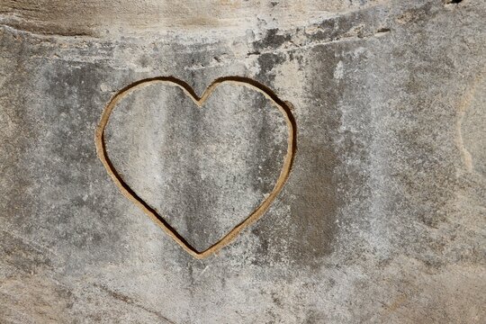 Heart shape carved into rough stone surface, symbolizing love, permanence, and ancient emotion. Natural light highlights the texture and detail of the rock.