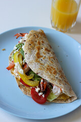 Tortilla wrap cooked on an egg base, filled with shrimp, avocado, bell pepper and spinach. Colorful and protein-packed side view of a healthy homemade meal