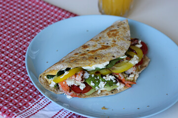 Side view of folded egg tortilla wrap filled with shrimp, avocado, feta, spinach and vegetables. Served on a blue plate. Healthy and colorful breakfast concept