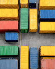 Aerial view of colorful shipping containers neatly arranged in rows on a gravel-covered freight yard.