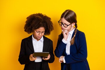 Two schoolgirls in uniforms studying together while using a tablet computer against a yellow background