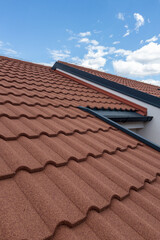 Terracotta roof tiles on a residential building under a bright blue sky with fluffy clouds