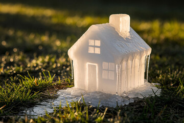 Melting ice cube house on grass under sun, symbolizing air conditioning, climate change, and environmental fragility