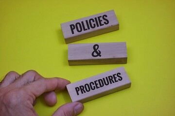 The Concept of policies and Procedures is Displayed on the Hand Holding a Wooden Block on a yellow...