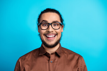 Portrait of a cheerful man in glasses and brown shirt against blue background, expressing joy and...
