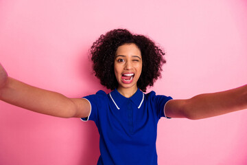 Young stylish woman with curly hair posing happily against a vibrant pink background with playful...
