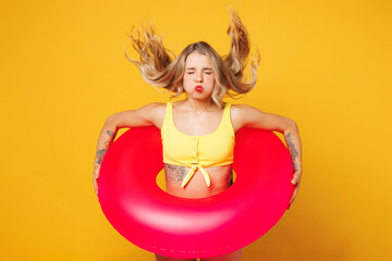 Young beautiful woman wear bikini swimsuit sunglasses rest near hotel pool hold pink rubber ring jump into water puff cheeks isolated on plain yellow background. Summer vacation sea sun tan concept.