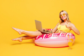 Full body young IT woman in bikini swimsuit rest near hotel pool lies on rubber ring work use...