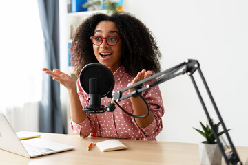 Excited African American woman recording podcast from home using professional microphone and laptop