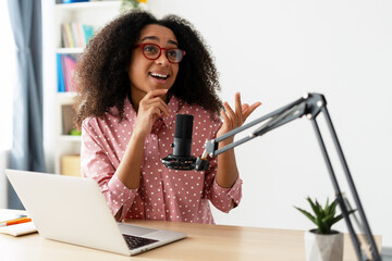 African American content creator wearing eyeglasses recording podcast using laptop and microphone