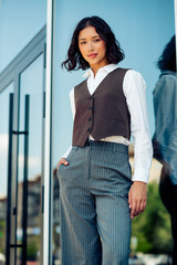Confident young businesswoman outdoors in stylish formal wear, standing by a modern glass building...