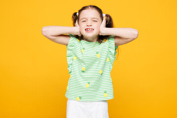 Little sad kid child girl 8-9 years old wears green t-shirt cover ears with hands fingers do not...