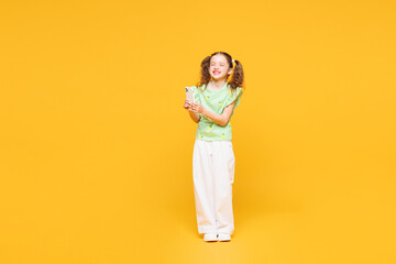 Full body little smiling kid child girl 8-9 years old wears green t-shirt hold in hand use mobile...