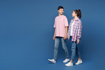 Full body profile young smiling happy couple two friends family man woman they wear pink casual clothes hold hands walk go stroll together isolated on plain blue background studio. Lifestyle concept.
