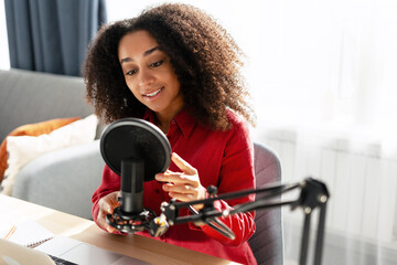 Smiling, beautiful woman recording podcast in home studio using professional microphone