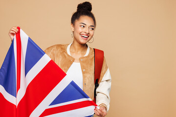Young happy smart girl student she wears casual clothes backpack bag hold big British flag look aside on area isolated on plain pastel light beige background. High school university college concept.
