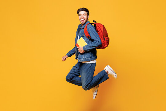 Full body side profile view smiling happy young boy student he wear denim casual clothes backpack bag hold books jump high isolated on plain yellow background. High school university college concept.
