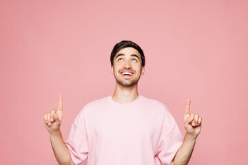 Young smiling Caucasian man he wear t-shirt casual clothes pointing index finer overhead indicate on workspace area isolated on plain pastel light pink background studio portrait. Lifestyle concept