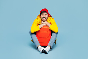 Traveler smiling man wears hat yellow casual clothes sit near bag look camera isolated on plain...