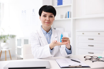 Portrait of professional ophthalmologist with eye drops at white table in clinic
