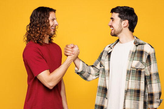 Young smiling happy two friends buddies men they wearing casual clothes together hold hands folded handshake gesture isolated on plain yellow orange color background studio portrait Lifestyle concept