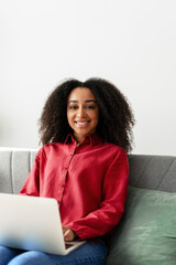 Smiling African American freelancer working from home using laptop on sofa