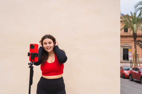 Curvy woman wearing sportswear recording a fitness video blog outdoors, using a smartphone on a tripod - Powered by Adobe