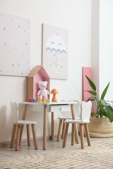 Small table, chairs and decor near white wall in stylish playroom. Interior design