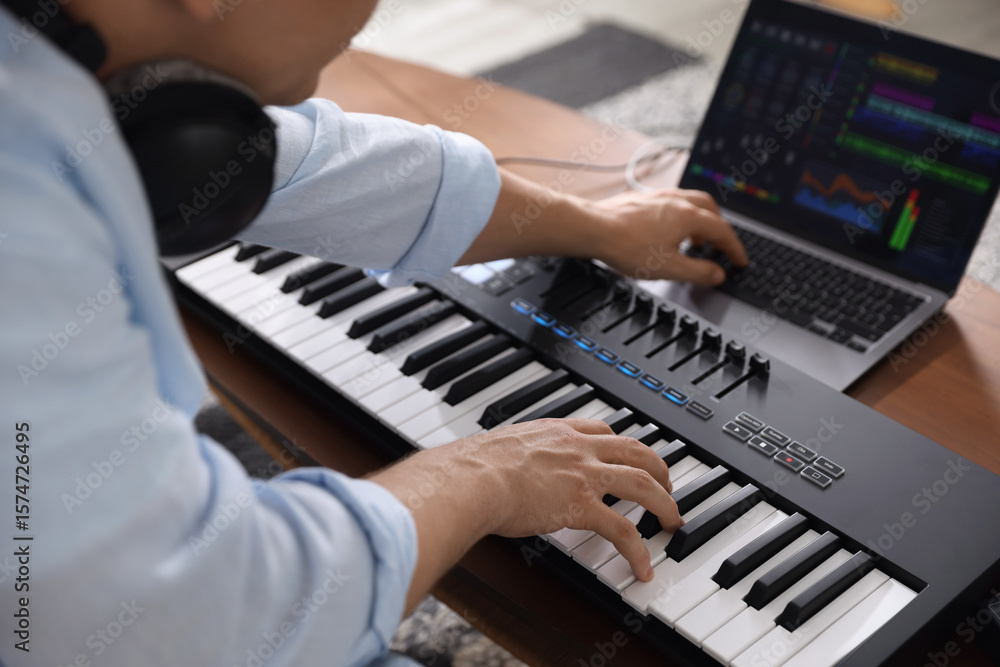 Poster man working with midi keyboard and laptop at table indoors, selective focus