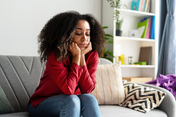 Sad woman sitting on sofa resting chin on hands at home
