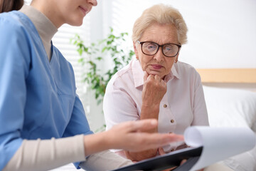 Obraz premium Nurse with clipboard examining senior woman indoors, closeup. Home health care service