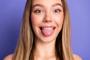 Portrait of a young woman smiling with braces, showcasing a playful expression by sticking out her...