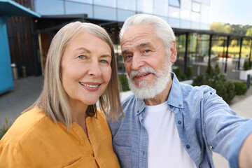 Lovely senior couple taking selfie near building outdoors
