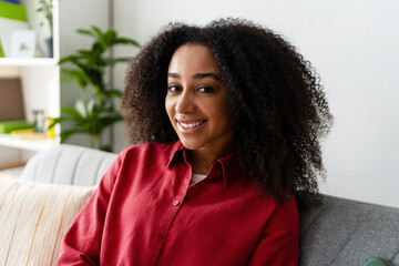 Young African American woman smiling and relaxing on comfortable sofa at home