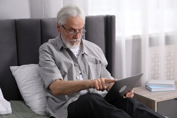 Senior man with vision problem using laptop on bed at home