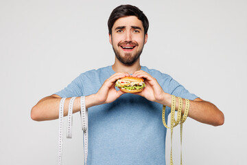 Young shocked sad man wears blue t-shirt casual clothes, tied hands with measure tape hold eat...