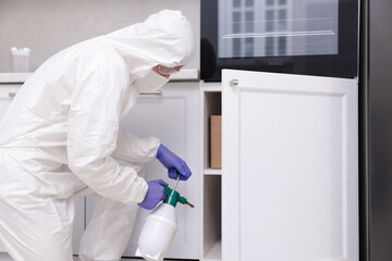 Pest control worker in protective suit spraying insecticide at home