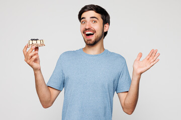 Young shocked surprised man wear blue t-shirt casual clothes hold in hand eat piece of cake spread...