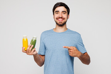 Young man wear blue t-shirt casual clothes hold in hand point on bottles of smoothie orange green...