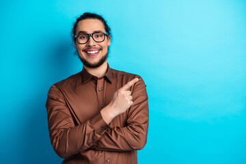 Cheerful young man in a brown shirt pointing with confidence against a bright turquoise background
